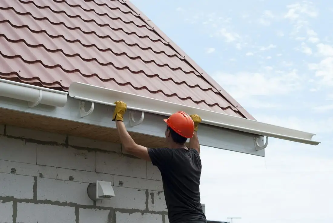 Worker professionally installing durable gutters on a residential roof to ensure proper water drainage and protection.