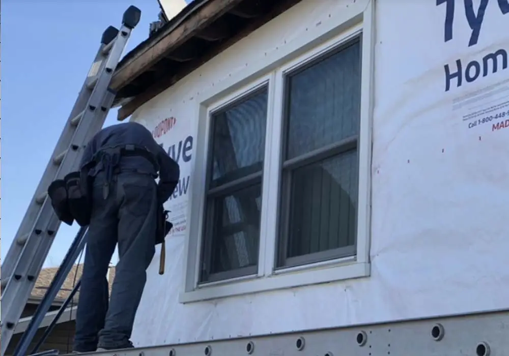 man working on the side of a house next to a ladder