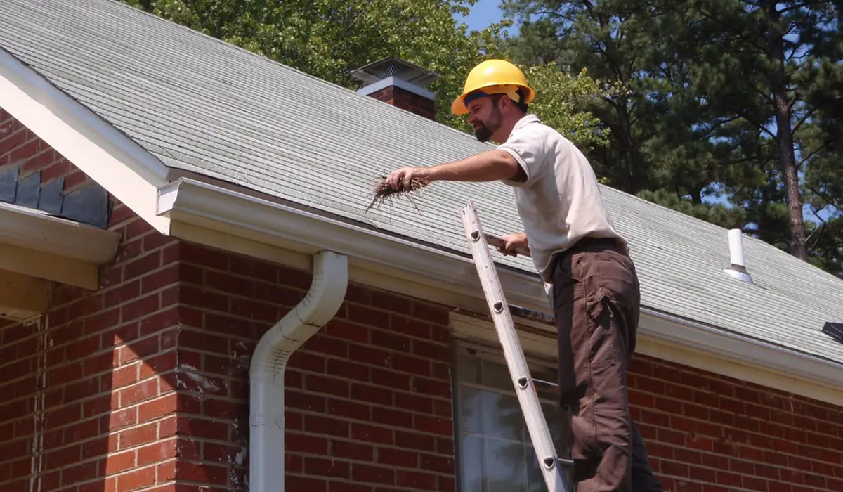 Worker clearing debris from gutters as part of winterizing your roof to prevent ice dam formation.