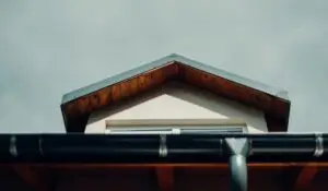 Roofing company fits rain gutter on a modern home with wooden eave.