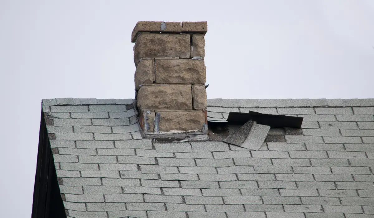 Visible storm damage requiring emergency roof repair in Lockport IL with lifted shingles near chimney on older asphalt roof.