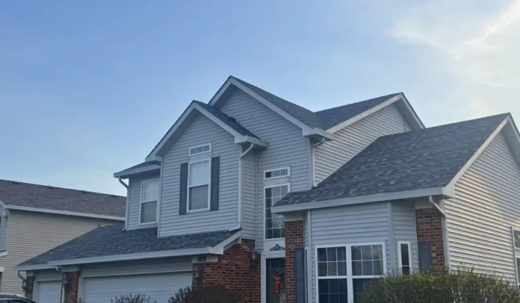 Vinyl siding installation Lockport home with gray siding, white trim, brick base, and gabled rooflines