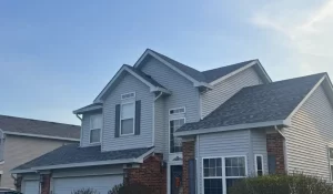 Vinyl siding installation Lockport home with gray siding, white trim, brick base, and gabled rooflines