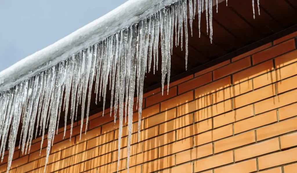Ice dam and icicles forming along roof edge showing a common gutter mistake during winter.